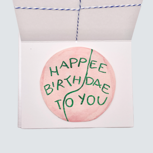 Folded handmade “Happee Birthdae” card with twine bow and rose gold foil border, blank inside.