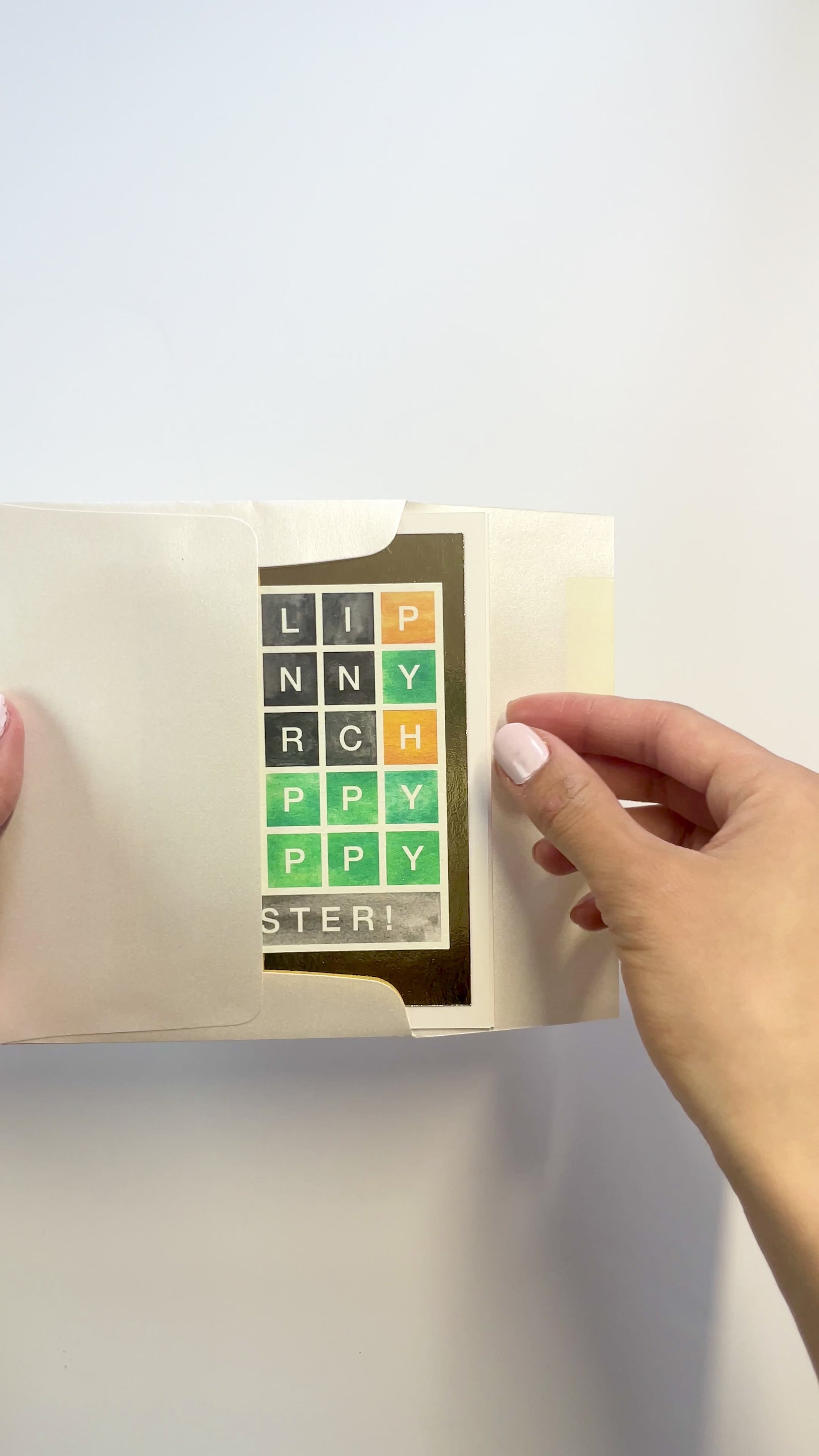 Hands opening an envelope to reveal a handmade Wordle-style Easter card with gold foil accents.