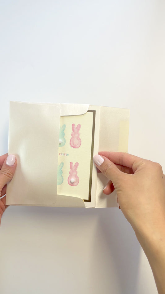 Hands opening an envelope to reveal a handmade Easter card with watercolor bunnies and pom-poms.