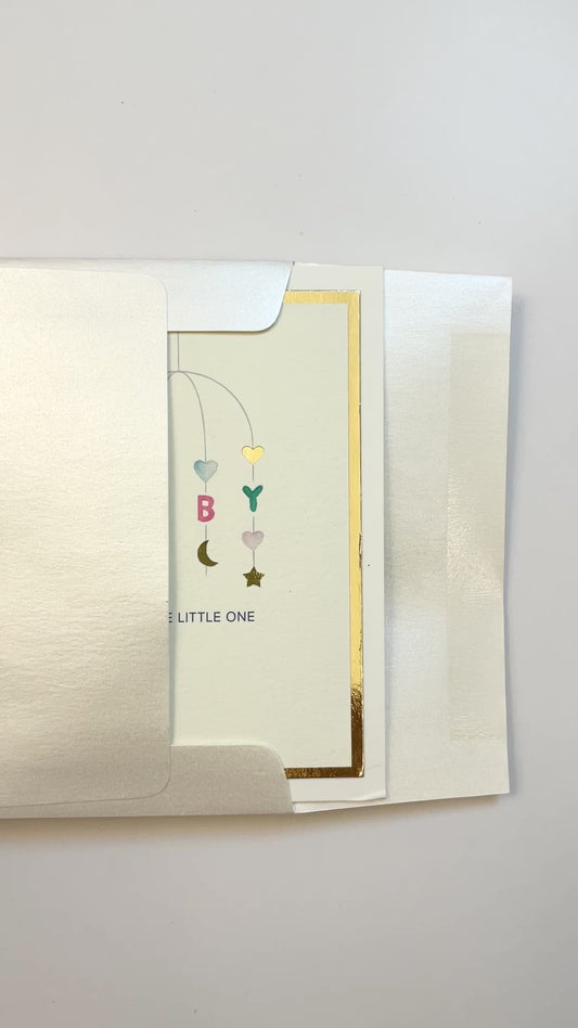 Hands opening an envelope to reveal a handmade neutral baby card with watercolor art and gold foil border.