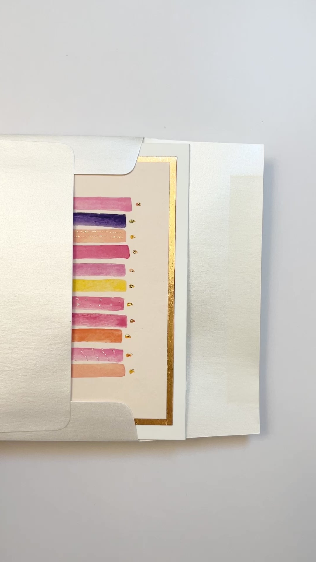 Hands opening an envelope to reveal a handmade pink and purple birthday candles card with rose gold foil.
