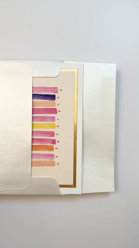 Hands opening an envelope to reveal a handmade pink and purple birthday candles card with rose gold foil.