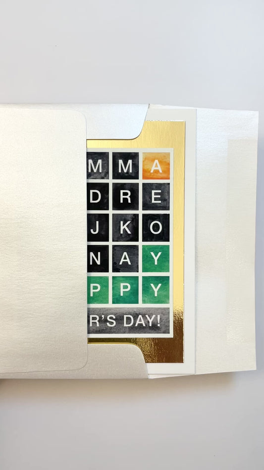 Hands opening an envelope to reveal a handmade Wordle-style Mother’s Day card with gold foil accents.