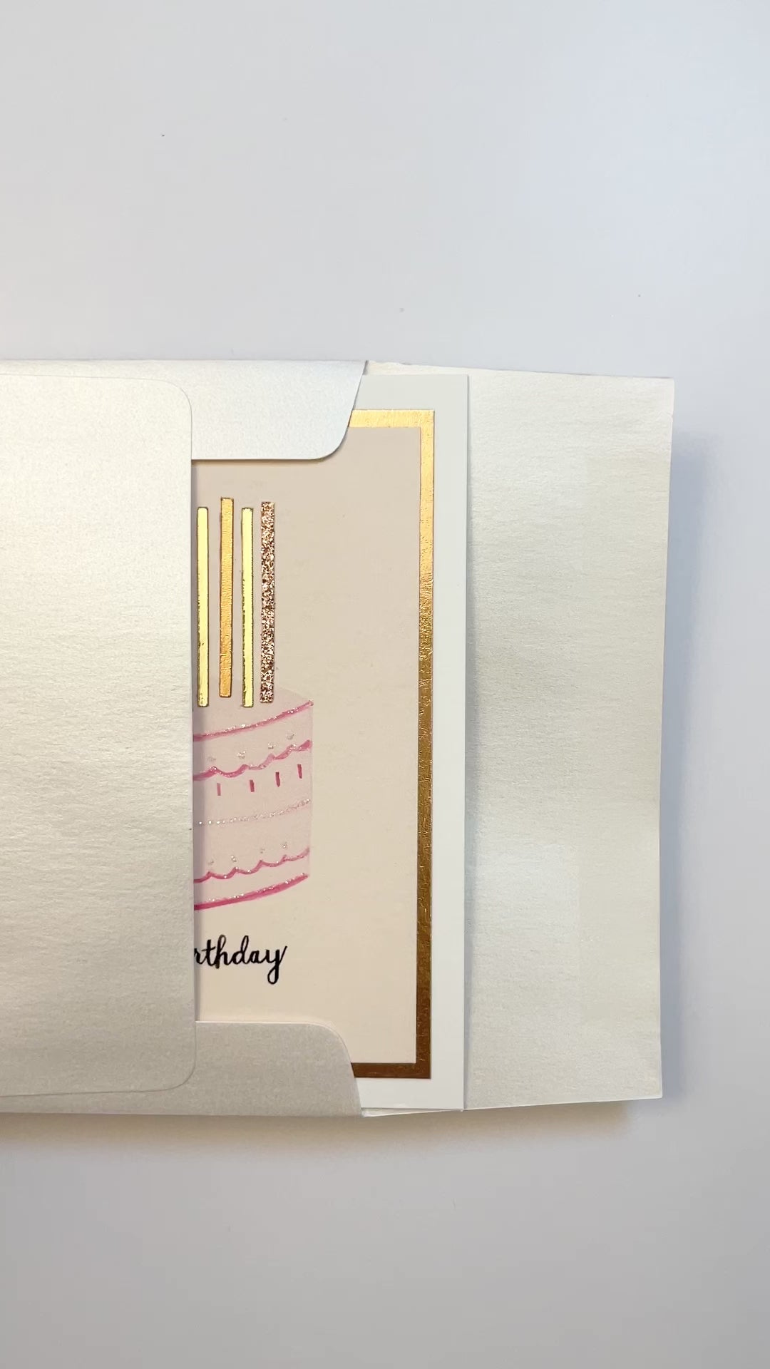 Hands opening an envelope to reveal a handmade pink birthday cake card with rose gold foil and glitter.