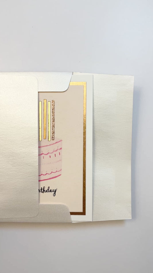 Hands opening an envelope to reveal a handmade pink birthday cake card with rose gold foil and glitter.