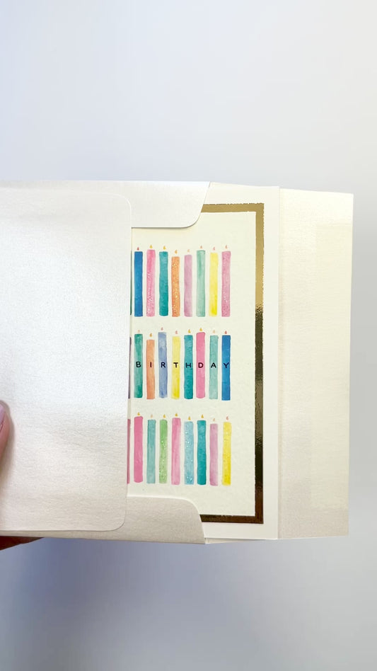 Hands opening an envelope to reveal a handmade birthday candles card with watercolor candles and gold foil details.