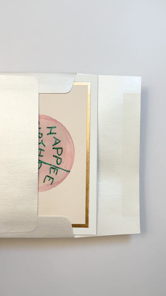 Hands opening an envelope to reveal a handmade “Happee Birthdae” flat card with rose gold foil details.