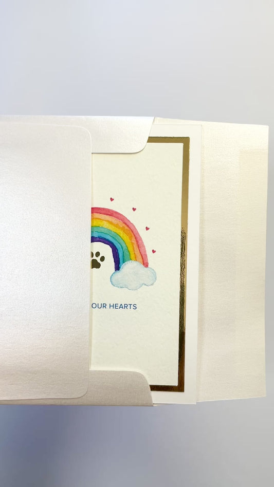 Hands opening an envelope to reveal a handmade pet loss sympathy card with rainbow and gold foil.