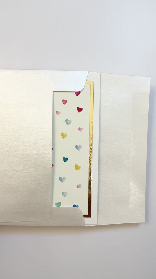 Hands opening an envelope to reveal a handmade thank you card with watercolor hearts and gold foil.