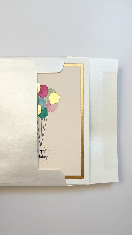 Hands opening an envelope to reveal a handmade birthday balloons card with rose gold foil and watercolor balloons.