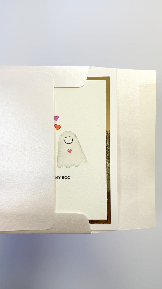 Hands opening an envelope to reveal a handmade “You’re My Boo” card with watercolor ghosts and gold foil.