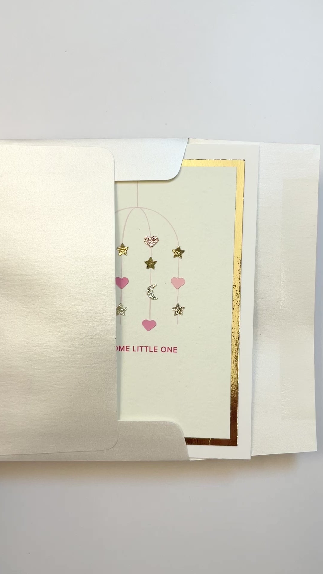 Hands opening an envelope to reveal a handmade pink baby card with gold foil and watercolor details.
