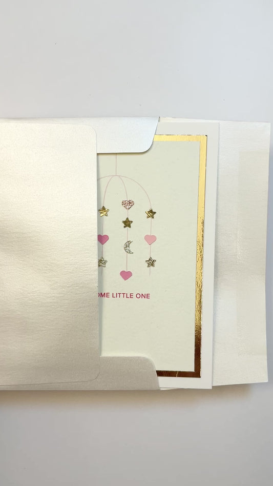 Hands opening an envelope to reveal a handmade pink baby card with gold foil and watercolor details.
