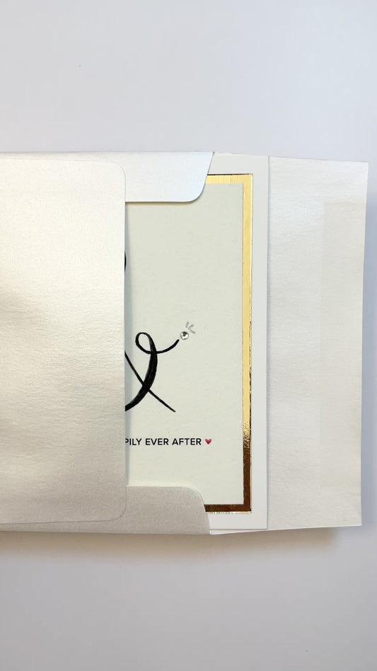 Hands opening an envelope to reveal a handmade wedding card with gold foil ampersand and silver rhinestone.