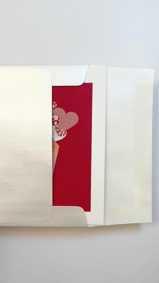 Hands opening an envelope to reveal a handmade origami bouquet card with paper flowers and washi details.