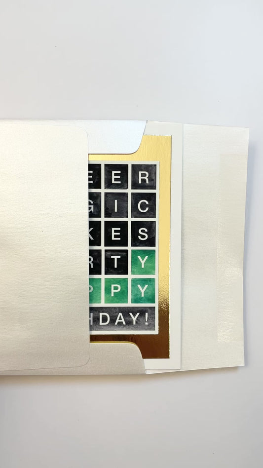 Hands opening an envelope to reveal a handmade Wordle-style birthday card with gold foil border.