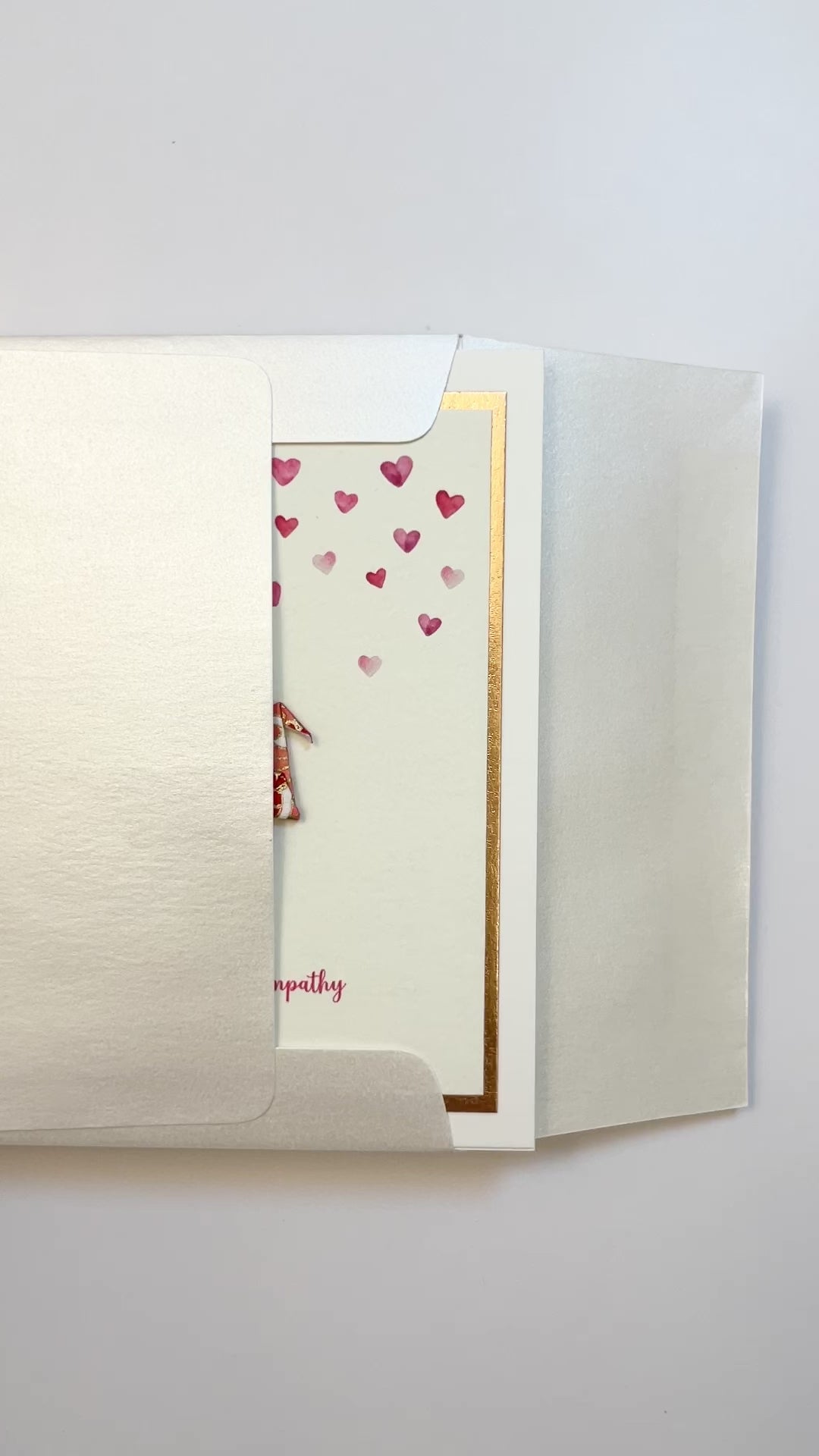 Hands opening an envelope to reveal a handmade sympathy card with origami crane and rose gold foil.