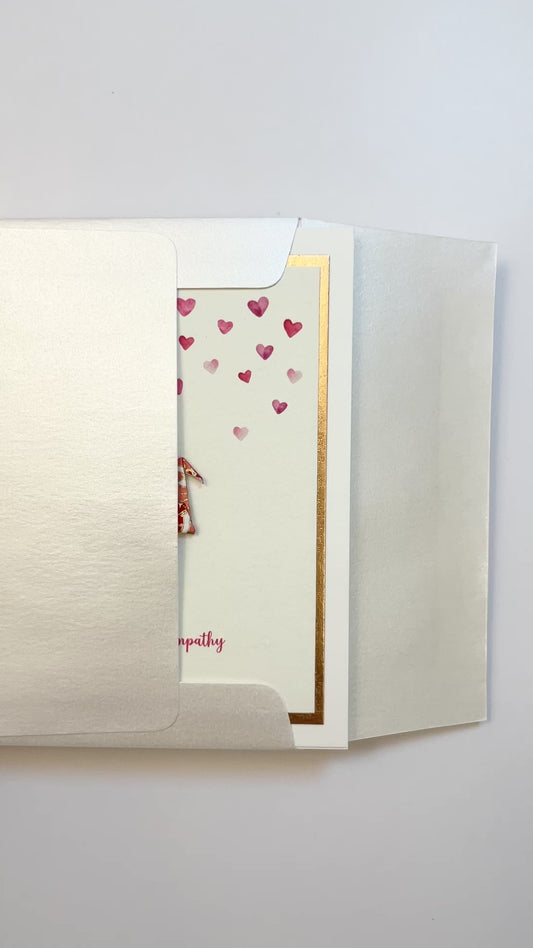 Hands opening an envelope to reveal a handmade sympathy card with origami crane and rose gold foil.