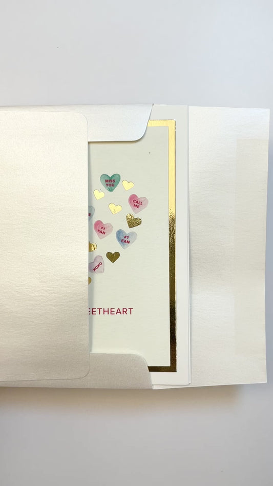 Hands opening an envelope to reveal a handmade Sweethearts card with watercolor hearts and gold foil.