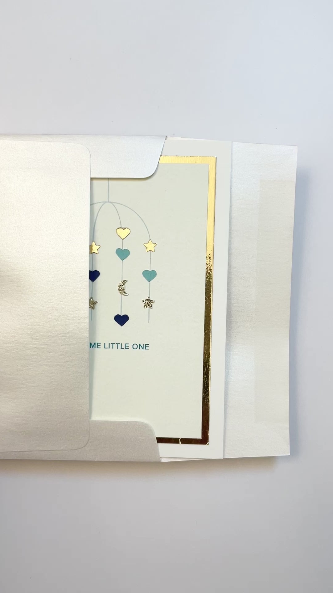 Hands opening an envelope to reveal a handmade blue baby card with gold foil and watercolor accents.