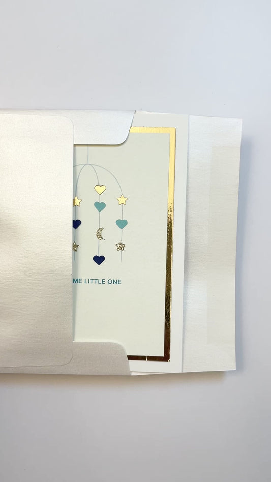 Hands opening an envelope to reveal a handmade blue baby card with gold foil and watercolor accents.