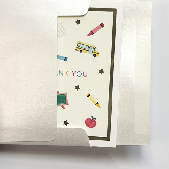 Person opening a handmade teacher thank you card with watercolor artwork and gold foil accents from a white envelope.
