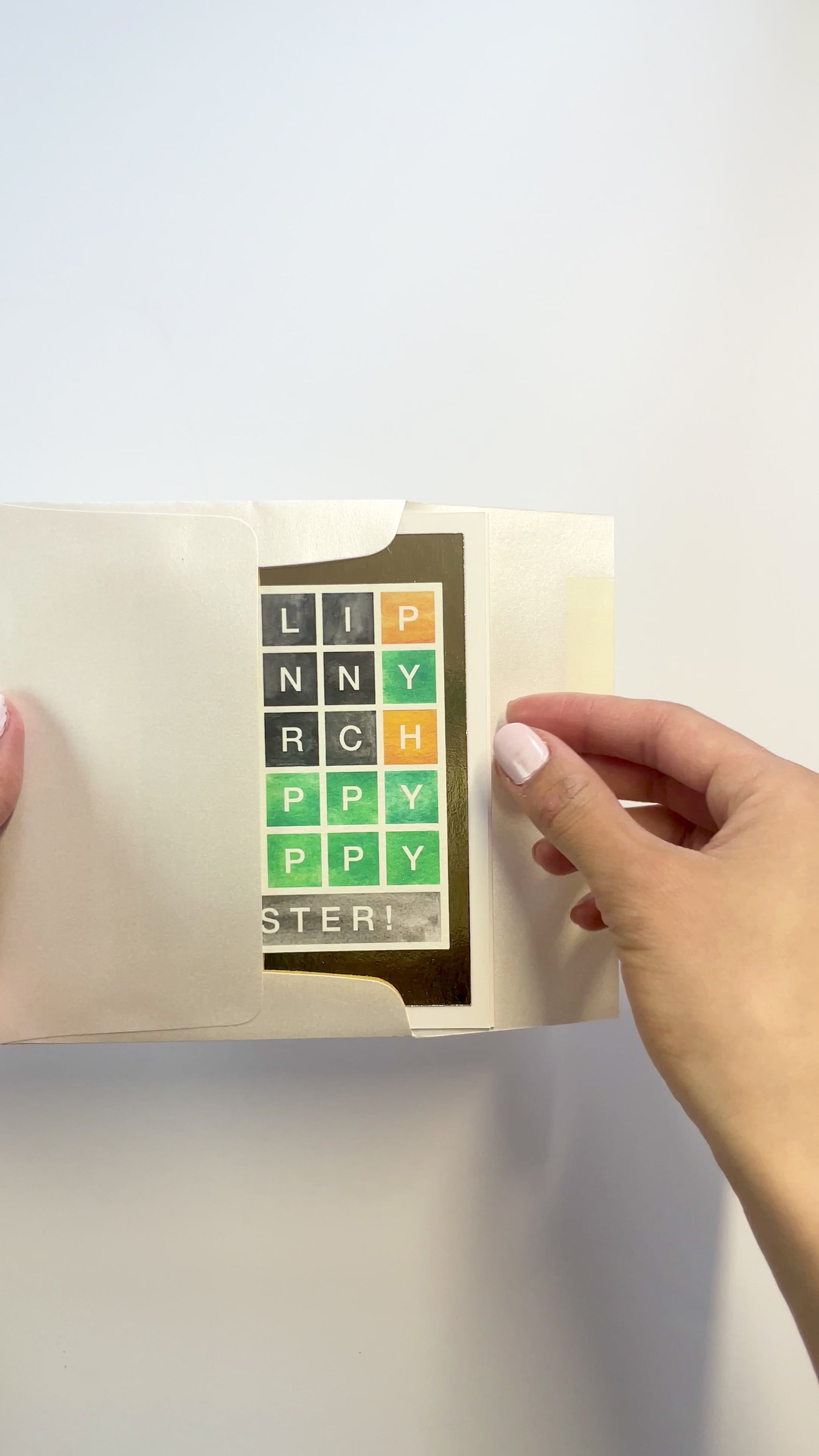 Hands opening an envelope to reveal a handmade Wordle-style Easter card with gold foil accents.