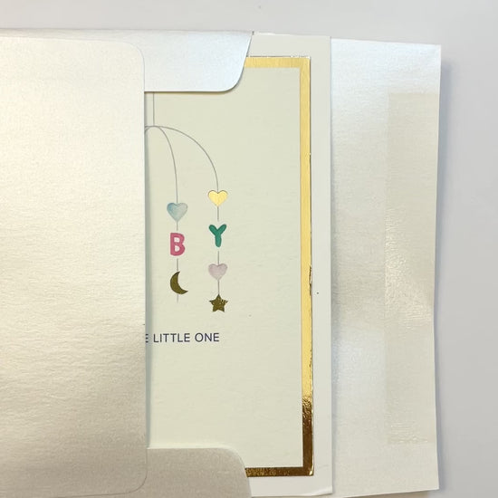 Hands opening an envelope to reveal a handmade neutral baby card with watercolor art and gold foil border.