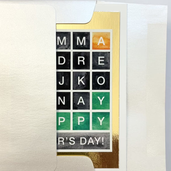 Hands opening an envelope to reveal a handmade Wordle-style Mother’s Day card with gold foil accents.