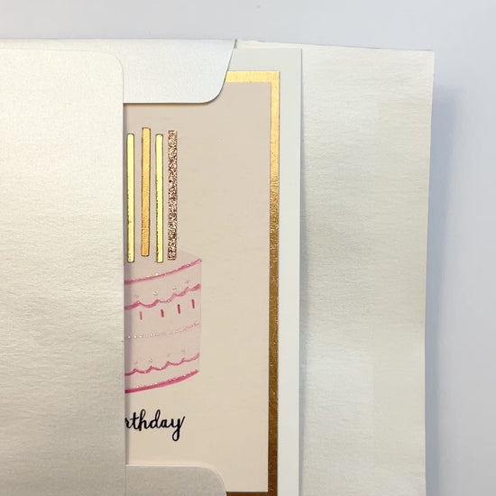 Hands opening an envelope to reveal a handmade pink birthday cake card with rose gold foil and glitter.