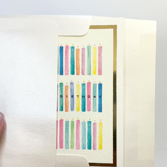 Hands opening an envelope to reveal a handmade birthday candles card with watercolor candles and gold foil details.