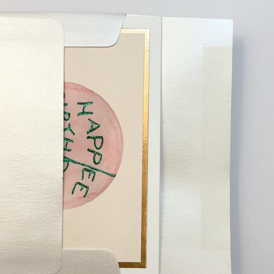 Hands opening an envelope to reveal a handmade “Happee Birthdae” flat card with rose gold foil details.
