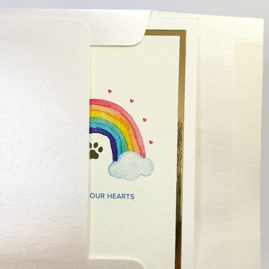 Hands opening an envelope to reveal a handmade pet loss sympathy card with rainbow and gold foil.