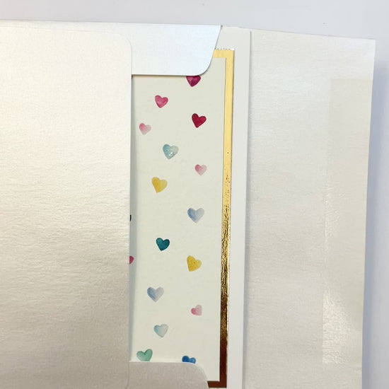 Hands opening an envelope to reveal a handmade thank you card with watercolor hearts and gold foil.