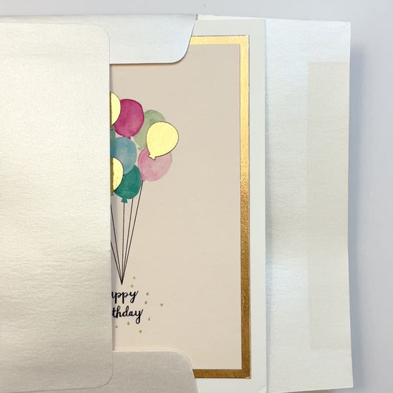 Hands opening an envelope to reveal a handmade birthday balloons card with rose gold foil and watercolor balloons.