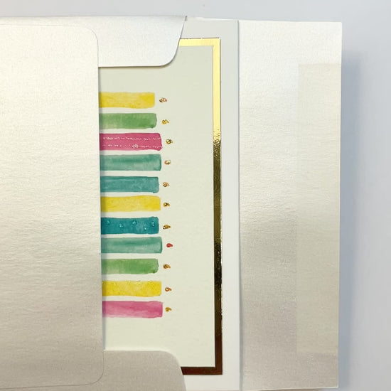Hands opening an envelope to reveal a handmade multicolor birthday candles card with watercolor art and gold foil accents.