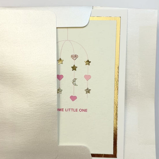 Hands opening an envelope to reveal a handmade pink baby card with gold foil and watercolor details.