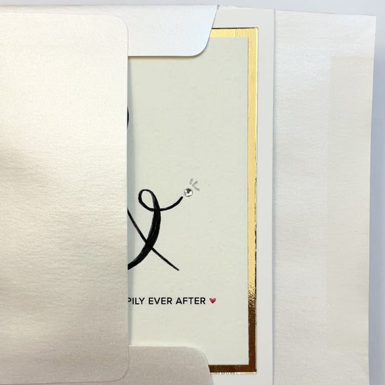 Hands opening an envelope to reveal a handmade wedding card with gold foil ampersand and silver rhinestone.