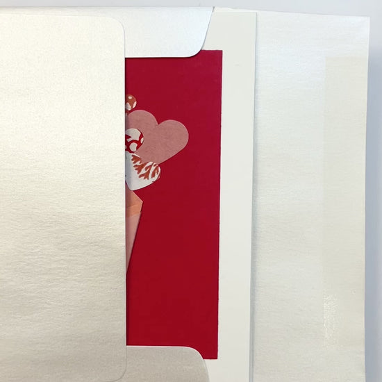 Hands opening an envelope to reveal a handmade origami bouquet card with paper flowers and washi details.