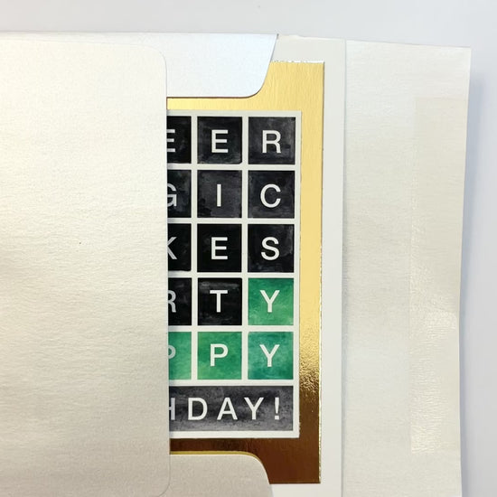 Hands opening an envelope to reveal a handmade Wordle-style birthday card with gold foil border.