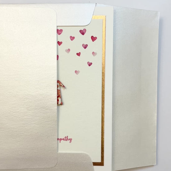 Hands opening an envelope to reveal a handmade sympathy card with origami crane and rose gold foil.