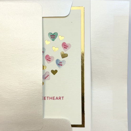 Hands opening an envelope to reveal a handmade Sweethearts card with watercolor hearts and gold foil.