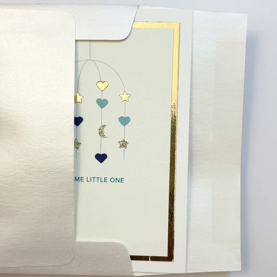 Hands opening an envelope to reveal a handmade blue baby card with gold foil and watercolor accents.